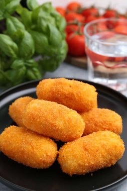 Lezzetli kızarmış kroketler, bir bardak su, domates ve fesleğen, yakın plan.