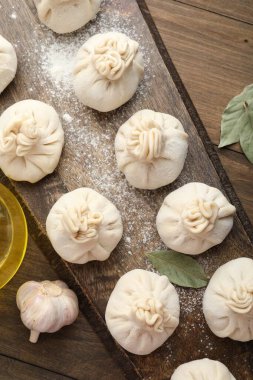 Tahta masa üzerinde un, sarımsak ve defne yapraklarıyla pişirilmemiş khinkaliler (hamur tatlısı)