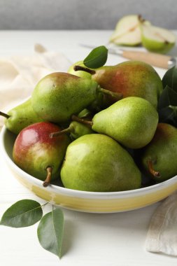 Taze armutlar kasede ve yeşil yapraklar beyaz ahşap masada, yakın plan.