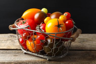 Tahta masada sepetin içinde farklı olgun domatesler, yakın plan.