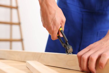 Profesyonel bir tamirci, kapalı alanda kıskaçlarla tahta çiviyi söküyor, yakın plan.