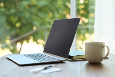 Bilgisayarı, kırtasiyeyi ve fincanı ahşap masada, bulanık yeşil arka planda, yakın plan