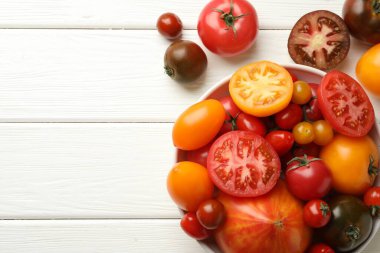 Beyaz ahşap masa üzerinde birçok farklı olgun domates, üst manzara. Metin için boşluk