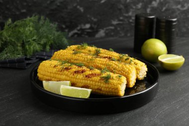 Lezzetli ızgara mısır koçanlarıyla siyah masada dereotu ve limon dilimleri.