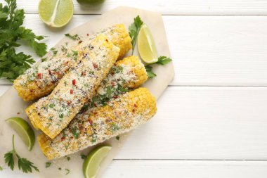 Lezzetli ızgara mısır koçanları maydanozlu, peynirli ve limon dilimli beyaz ahşap masa, düz yatak. Metin için boşluk