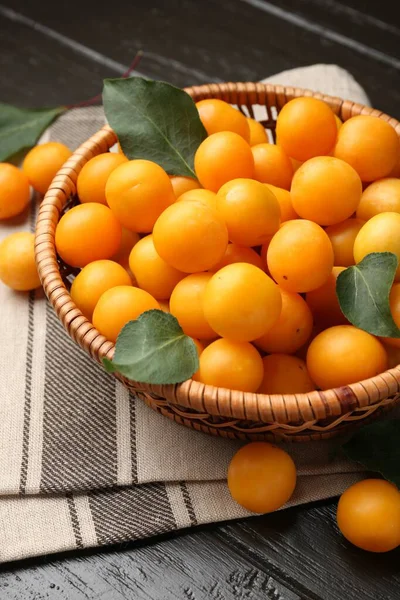 Olgun sarı kiraz erikleri ve koyu ahşap masada yapraklar, yakın plan.