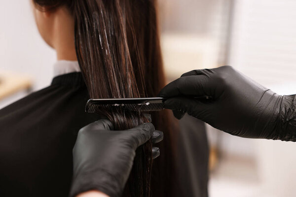 Hairdresser laminating woman's hair in salon, closeup