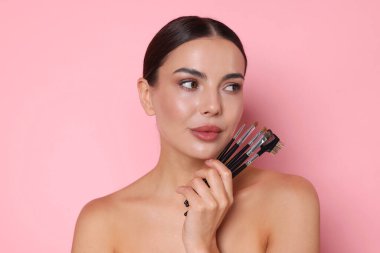 Pembe bir arka plan üzerinde makyaj fırçaları ile güzel kadın