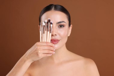 Kahverengi arka planda makyaj fırçası olan güzel bir kadın.