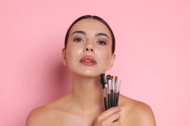 Pembe bir arka plan üzerinde makyaj fırçaları ile güzel kadın