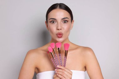 Açık gri arka planda makyaj fırçası olan güzel bir kadın.
