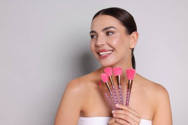 Açık gri arkaplanda makyaj fırçaları olan güzel bir kadın, metin için boşluk