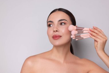 Açık gri arkaplanda makyaj fırçaları olan güzel bir kadın, metin için boşluk