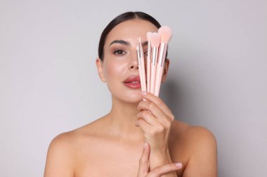 Açık gri arka planda makyaj fırçası olan güzel bir kadın.