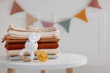 İçerideki beyaz masada temiz bebek kıyafetleri ve aksesuarlar yığını, yakın plan. Metin için boşluk