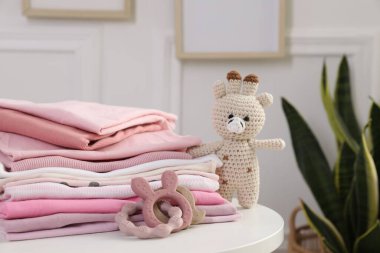 İçerideki beyaz masada temiz bebek kıyafetleri ve oyuncaklar yığını, yakın plan.