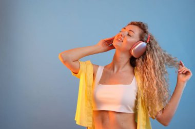 Kulaklıkla müzik dinleyen ve açık mavi arka planda dans eden mutlu kadın. Metin için boşluk