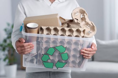 Geri dönüşüm. Kapalı alanda farklı atık kağıtları olan plastik kutu tutan adam.