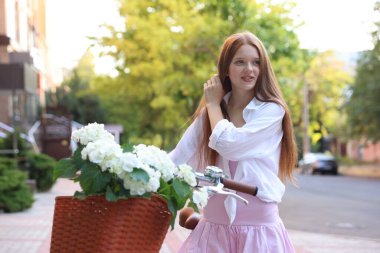 Bisikletin yanında güzel bir genç kız ve şehir caddesinde bir sepet çiçek.