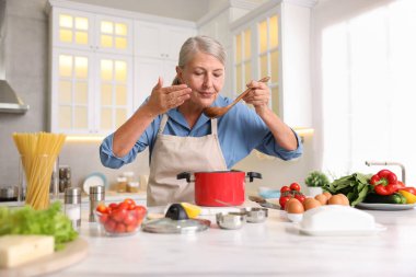 Üst düzey kadın mutfaktaki beyaz mermer masada yemek pişiriyor.