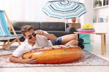 Güneş gözlüklü mutlu adam ve şişme yüzüklü paletler evde yerde eğleniyor. Denizde tatilin hayalini kuruyorum.