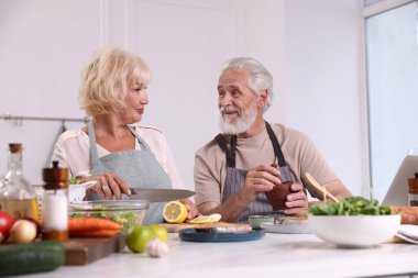 Yaşlı çift içeride birlikte yemek pişiriyor.