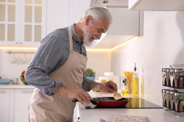 Mutfaktaki mutfağın tepesinde yaşlı bir adam yemek pişiriyor.