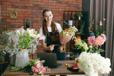 Profesyonel çiçekçi dükkandaki ahşap masada çiçek buketi yapıyor.
