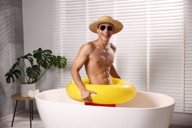 Güneş gözlüklü, hasır şapkalı, şişme yüzüklü, evinde küvette dinlenen mutlu bir adam. Denizde tatilin hayalini kuruyorum.