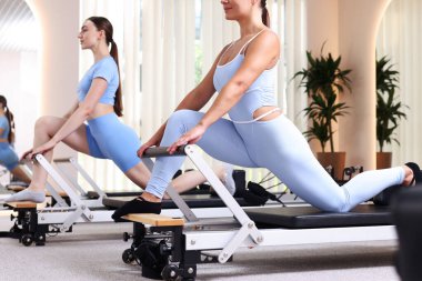 Stüdyoda reformcular üzerinde egzersiz yapan kadın ve pilates eğitmeni.