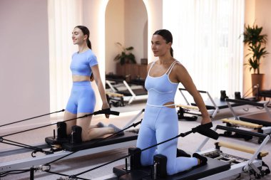 Stüdyoda reformcular üzerinde egzersiz yapan kadın ve pilates eğitmeni.