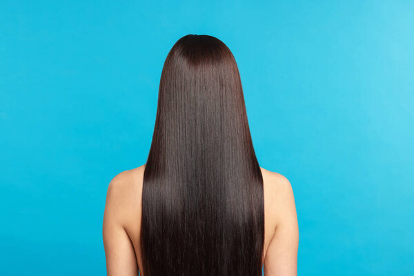 Женщина с красивыми гладкими волосами после процедуры ламинирования на светло-голубом фоне, вид сзади