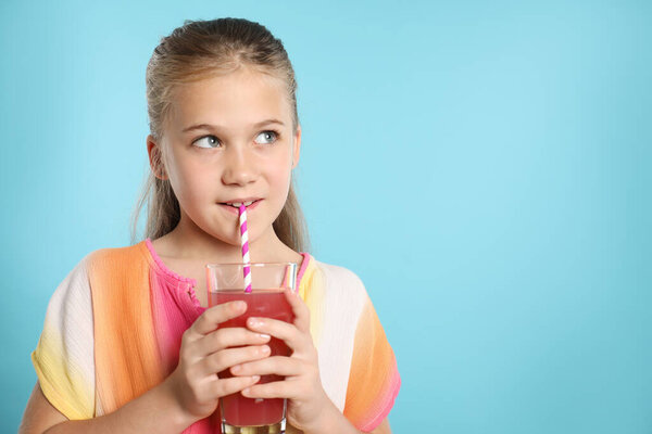 Девочка пьет сок через соломинку на голубом фоне, место для текста