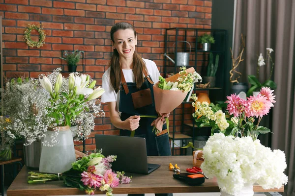 Profesyonel çiçekçi dükkandaki ahşap masada çiçek buketi yapıyor.