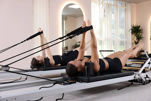 Stüdyoda reformcular üzerinde egzersiz yapan kadın ve pilates eğitmeni.