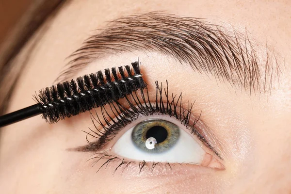 Bir kadın kirpiklerine rimel sürüyor, yakın plan.