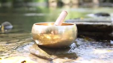 Tibet şarkı kasesi. Nehir kenarındaki taşın üzerinde tokmak var. Yakın plan. Kamera hareket ediyor