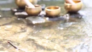 Nehirde taşların üzerinde tokmak olan Tibet şarkı kaseleri. Kamera yukarı hareket ediyor