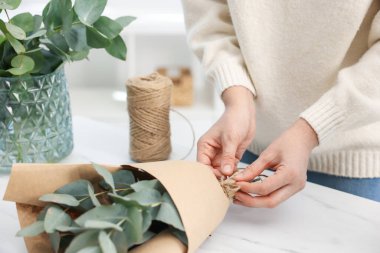 Çiçekçinin beyaz mermer masasında okaliptüs dallarından güzel bir buket yapıyor.