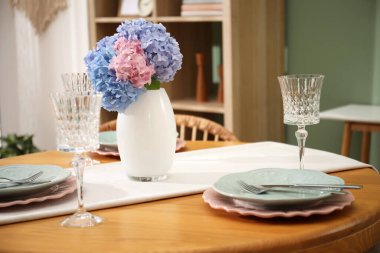 Yemek odasındaki ahşap masada, tabak ve vazo çiçekli şık bir ortam. İç tasarım