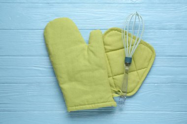 Yeşil fırın eldiveni, tutkal ve açık mavi ahşap masa üzerinde çırpma, düz uzanma