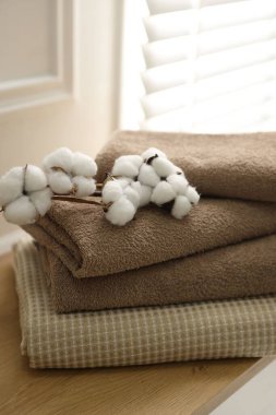 Evdeki ahşap masada temiz havlular ve pamuk çiçekleri yığını.