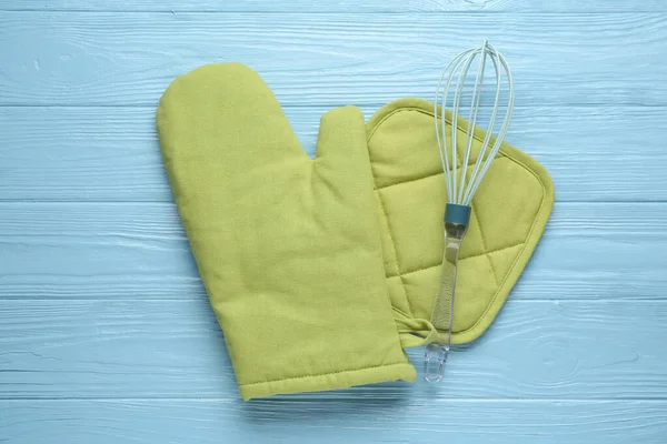 Yeşil fırın eldiveni, tutkal ve açık mavi ahşap masa üzerinde çırpma, düz uzanma