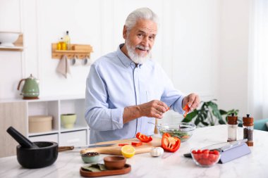 Mutfaktaki beyaz mermer masada yaşlı bir adam yemek pişiriyor.