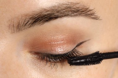 Bir kadın kirpiklerine rimel sürüyor, yakın plan.