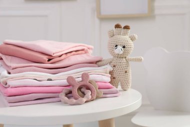 İçerideki beyaz masada temiz bebek kıyafetleri ve oyuncaklar yığını, yakın plan.