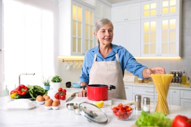 Üst düzey kadın mutfaktaki beyaz mermer masada yemek pişiriyor.