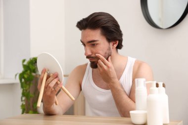 Akne sorunu olan genç bir adam içerideki masaya aynaya bakıyor.