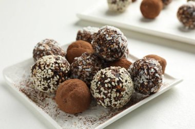 Beyaz masada kakao tozu, fındık ve susam tohumlu lezzetli çikolata şekerleri, yakın plan.