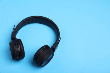 Açık mavi arka planda bir çift şık siyah kulaklık. Metin için boşluk